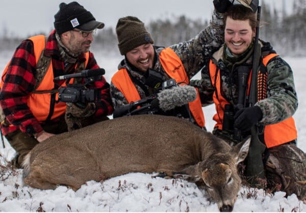 3 hunters kneeling beside a dead deer