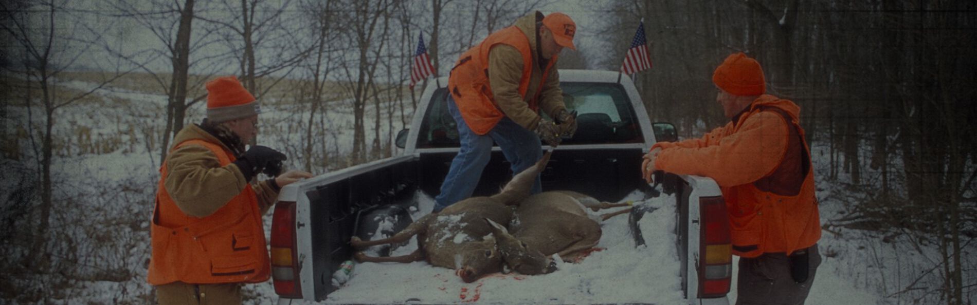 men loading a dead deer into a pick up truck bed
