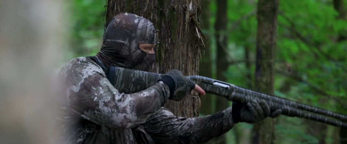 camoflaged hunter reading a shotgun in a tree line
