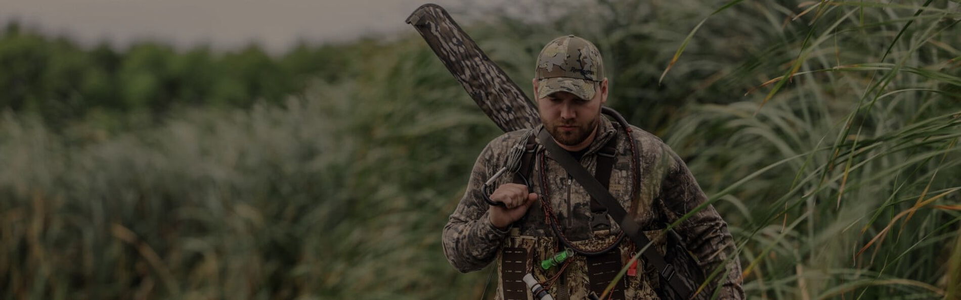 waterfowl hunter walking through water with a rifle bag on his back