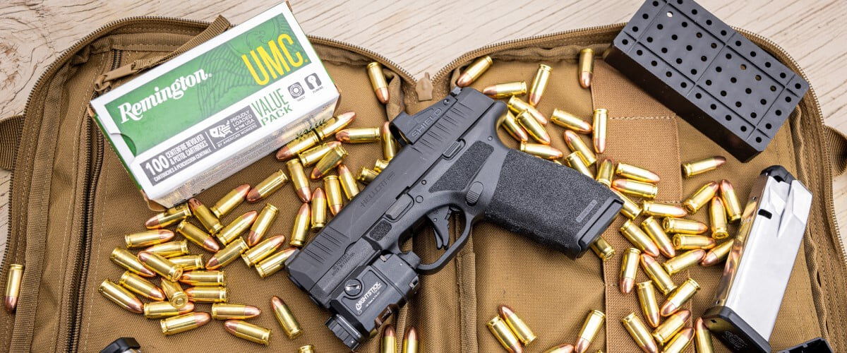 Remington UMC box with UMC cartridges scattered around a handgun, and magazine inside a pistol bag