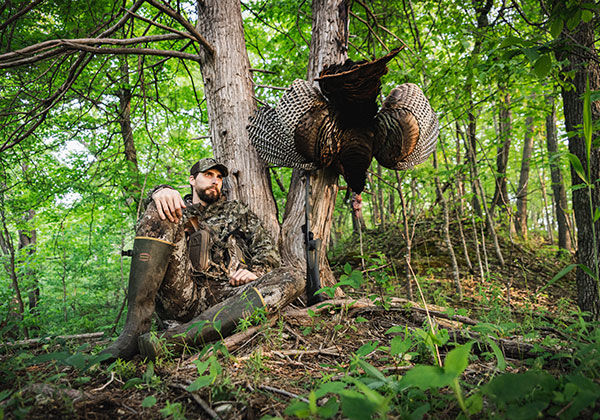 hunter next to a turkey hanging from a tree