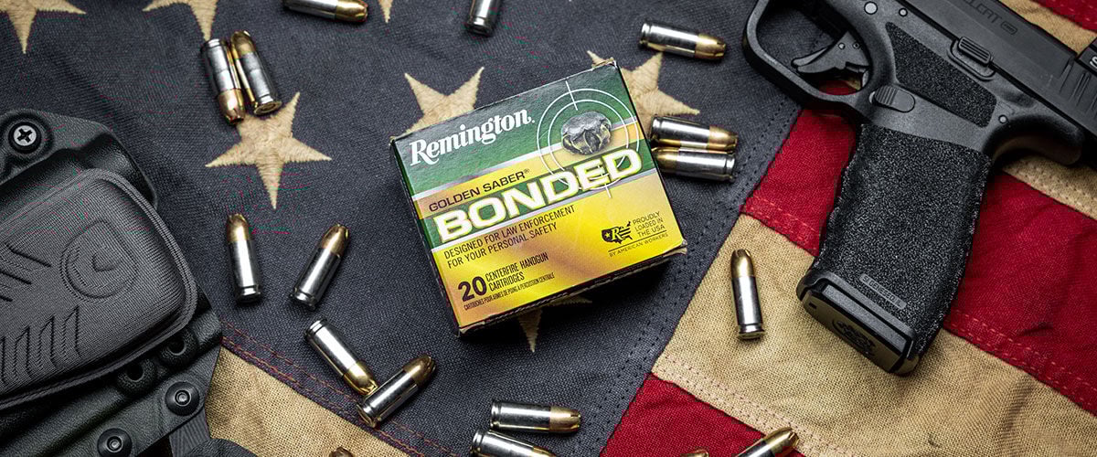 Golden Saber Bonded box and cartridges laying on a flag with a pistol and holster