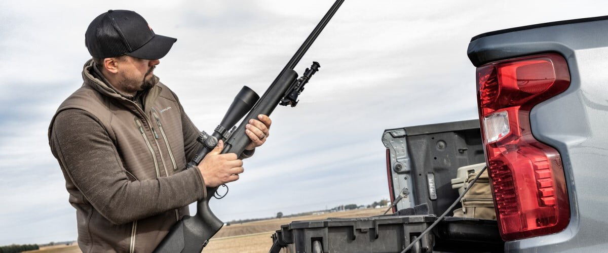 shooter standing by a truck tailgate and holding a rifle