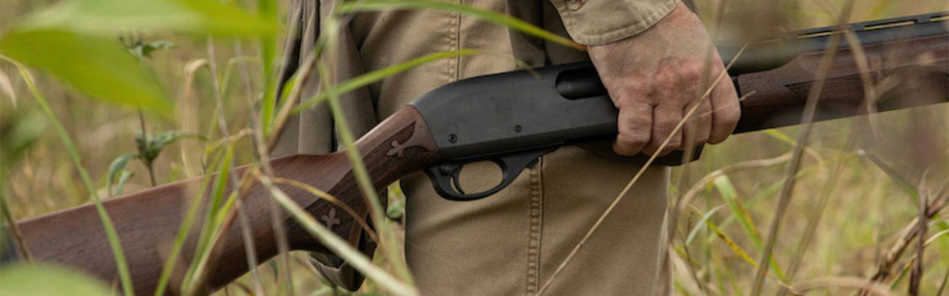 hunter standing in tall grass holding his shotgun at his side