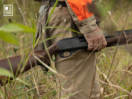hunter standing in tall grass holding his shotgun at his side