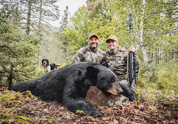 2 hunters kneeling behind a dead black bear