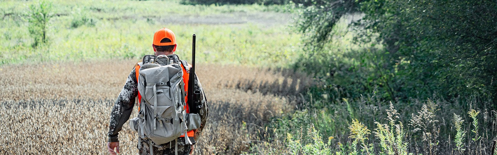 hunter walking through tall trass with a backpack and a rifle