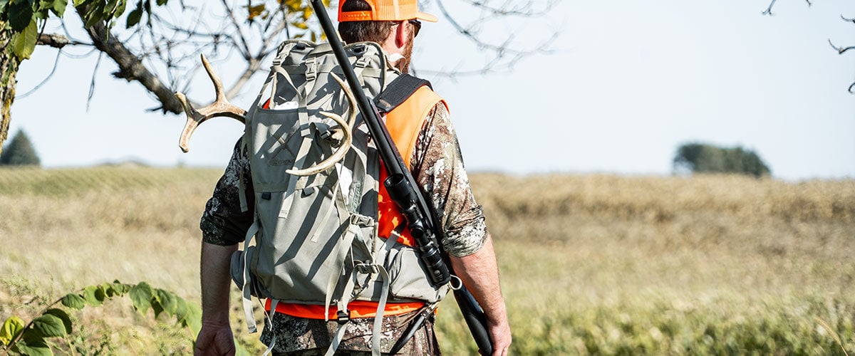 huting walking in a field with a backpack and a rifle