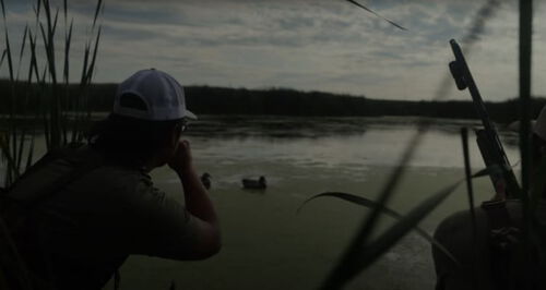 Jon using a duck call next to a lake with duck decoys