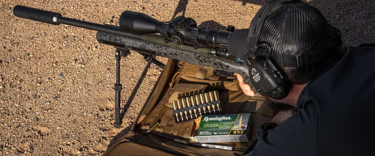 shooter looking down a rifle scope while laying on the ground