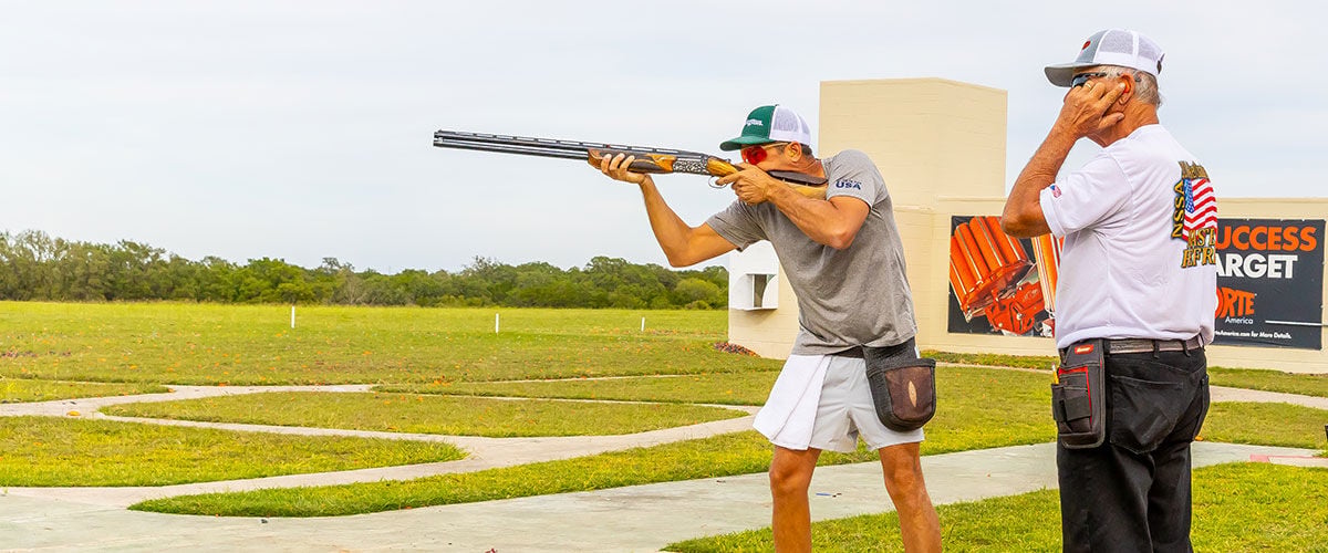 shooter aiming shotgun with person standing behind them 