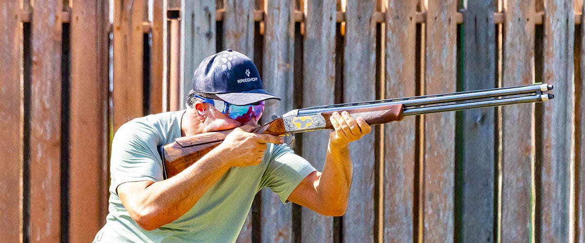 shooter aiming shotgun in front of a wood fence