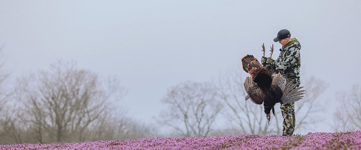 hunter holding turkey in a pink flower field