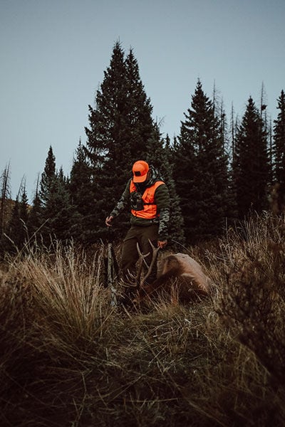 hunter standing in tall grass with a dead caribou