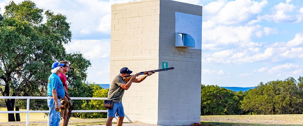 shooter aiming shotgun at skeet station