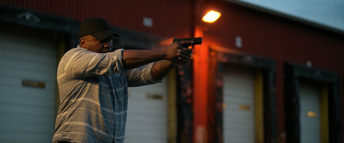 person aiming handgun at dusk in front from a warehouse