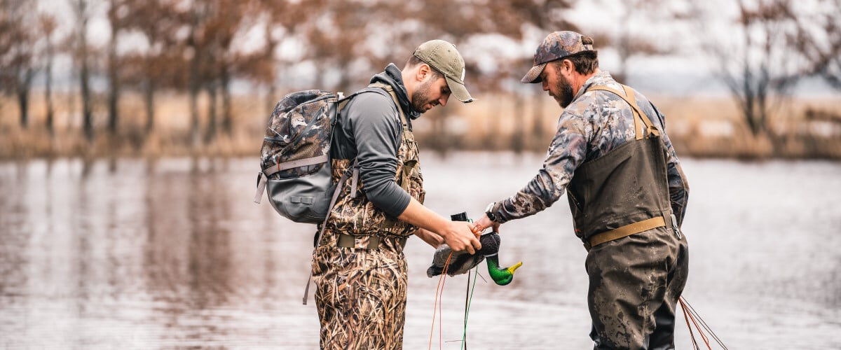 two hunters setting up waterfowl decoys on a pond