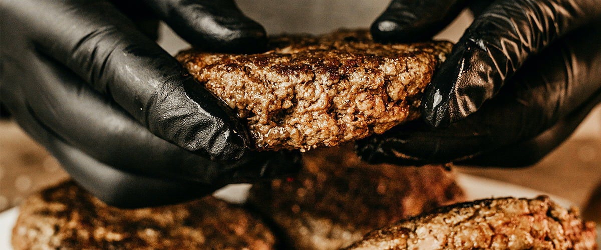 cooked burger being help in someones hands above a plate full of cooked burgers